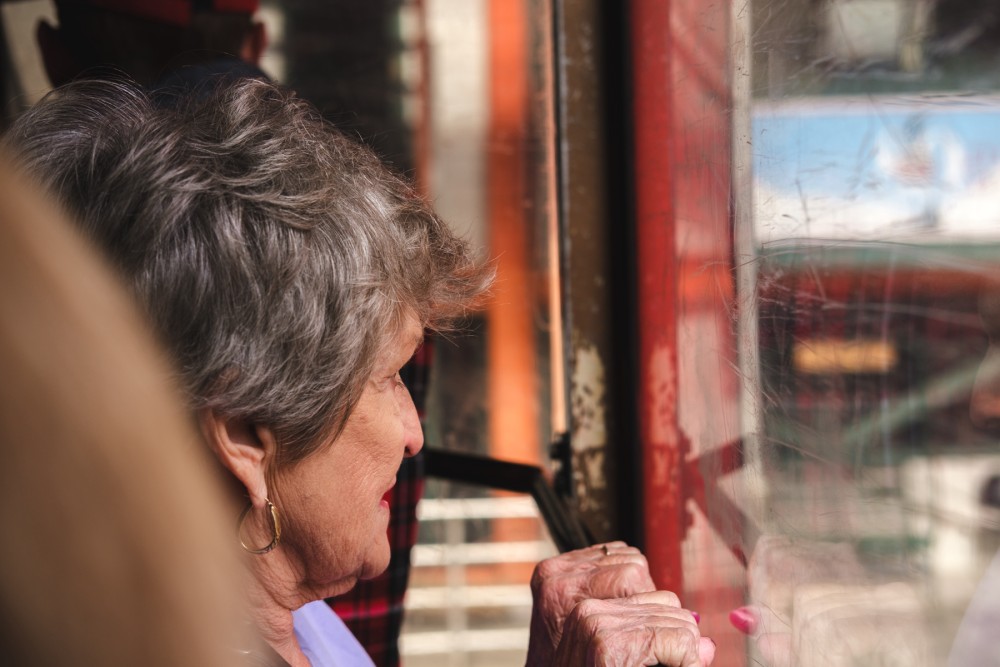 A woman with gray hair looking out of the window of a red cable car, with reflection visible on the glass.