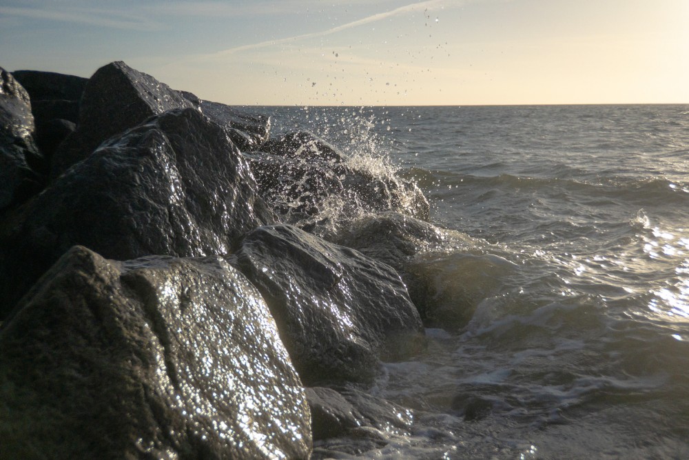Waves crashing against rocky shore with early morning sunlight reflecting on the water.