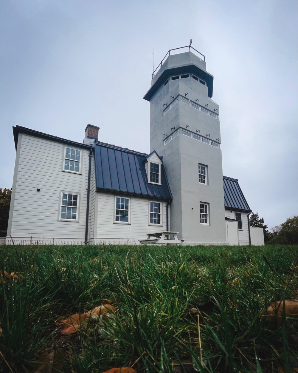 White building with blue roofs and a tower under a cloudy sky, surrounded by green grass.