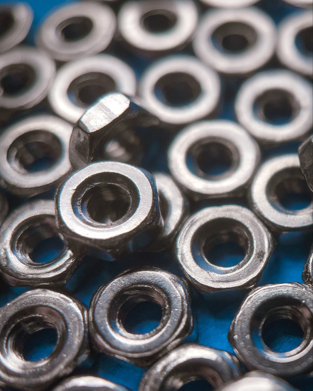 Macro photo of a loosely arranged grid of metal nuts with a few on top of the main grid. A blue background can be seen between some of the nuts.