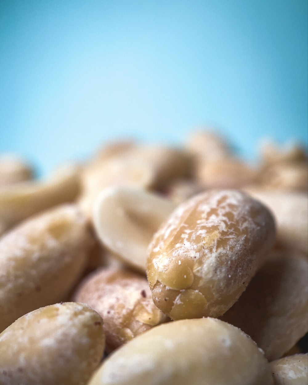Macro photo of a pile of shelled and sliced peanuts in front of a blurred, light blue background.