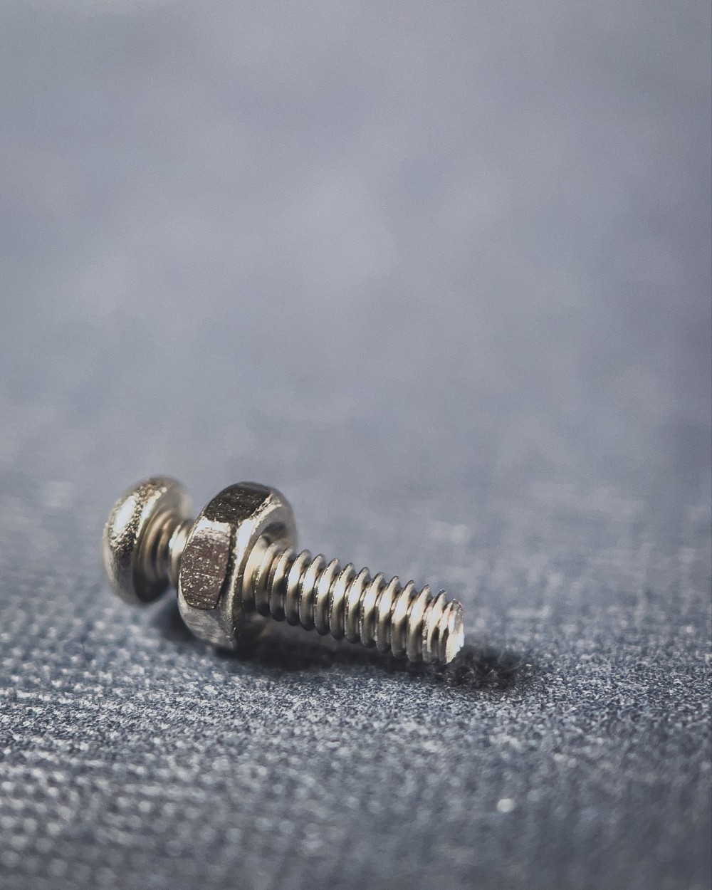 Macro photo of a single bolt with a nut almost all of the way at the top on a pale denim colored and textured surface.