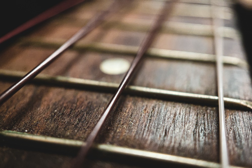 Close up photo of the strings of a ukulele. Strings are various shades of brown on top of the lighter brown neck of the instrument.
