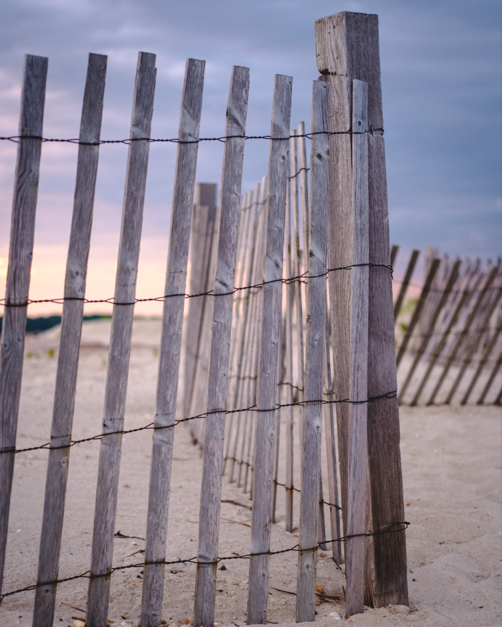A weathered wooden fence on a sandy beach with a sunrise sky in the background.