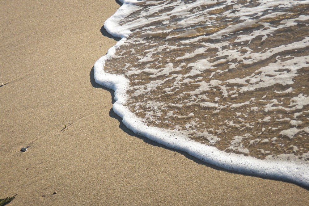 Close up of sea foam on the edge of a smooth sandy beach with gentle waves washing ashore.