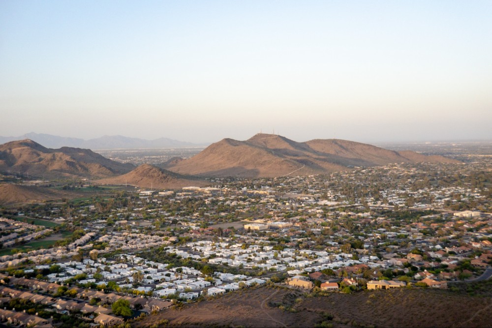 Aerial view of a residential area with houses spread out at the foothills of a mountain range just after sunrise.