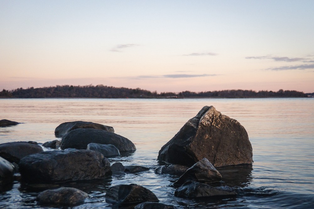 Rocks protruding from calm waters with a dawn sky in the background.